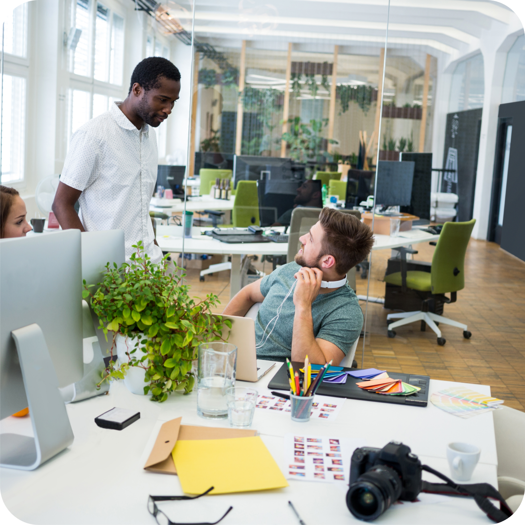 Two colleagues at FIXATE engaged in discussion about customer care in a modern, creative office with plants, design materials, and a camera on the desk.